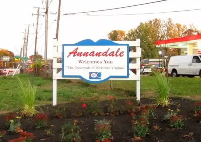 A welcoming sign reading "Annandale Welcomes You, The Crossroads of Northern Virginia" stands proudly near a gas station and lush greenery, showcasing fresh asphalt paving.