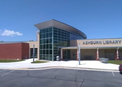 Modern library building with large glass windows, a curved roof, and a sign reading "Ashburn Library." The pristine paving around the building enhances its contemporary appeal, making it a standout architectural gem in VA.